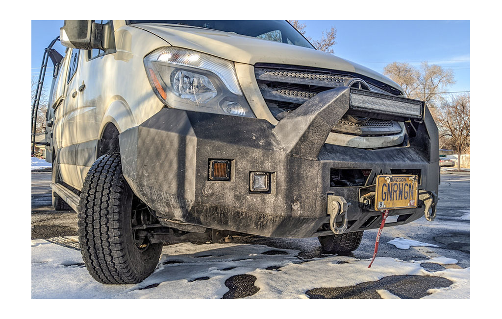 Front end of Winnebago Revel with snow tires and front bumper with added lights and winch.