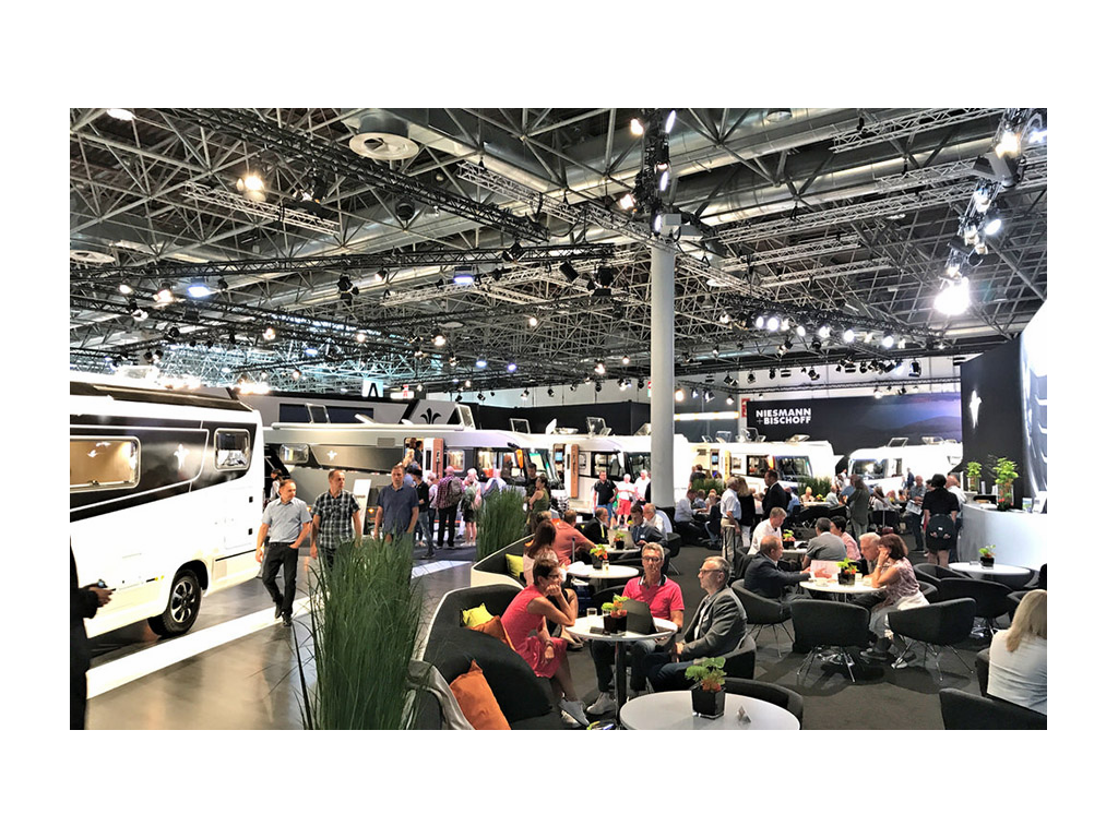 People gathered around tables and standing next to RVs at Caravan Salon in 2017