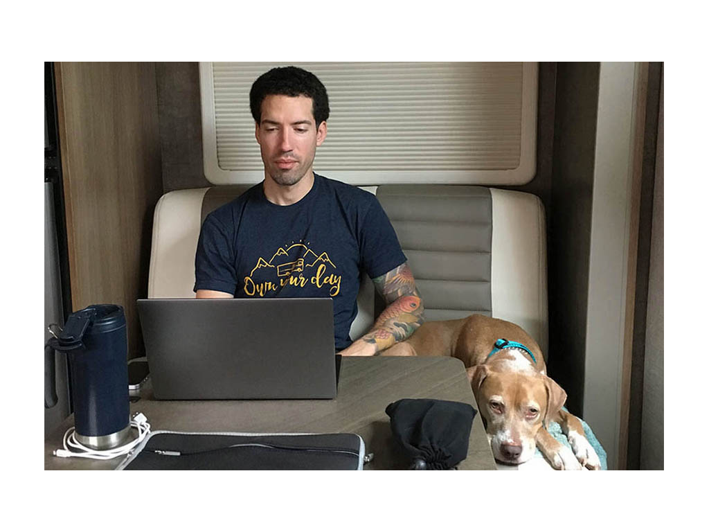 Jon sitting at dinette working on laptop. Large brown dog sitting nearby