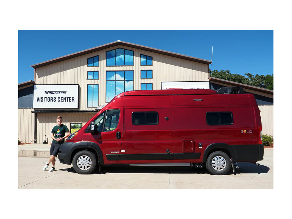 Mikah standing next to red Solis in front of Winnebago Visitors Center