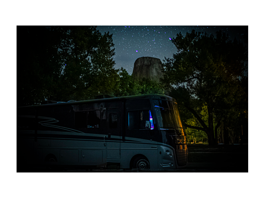 Adventurer next to Devils Tower National Monument with stars in sky at night