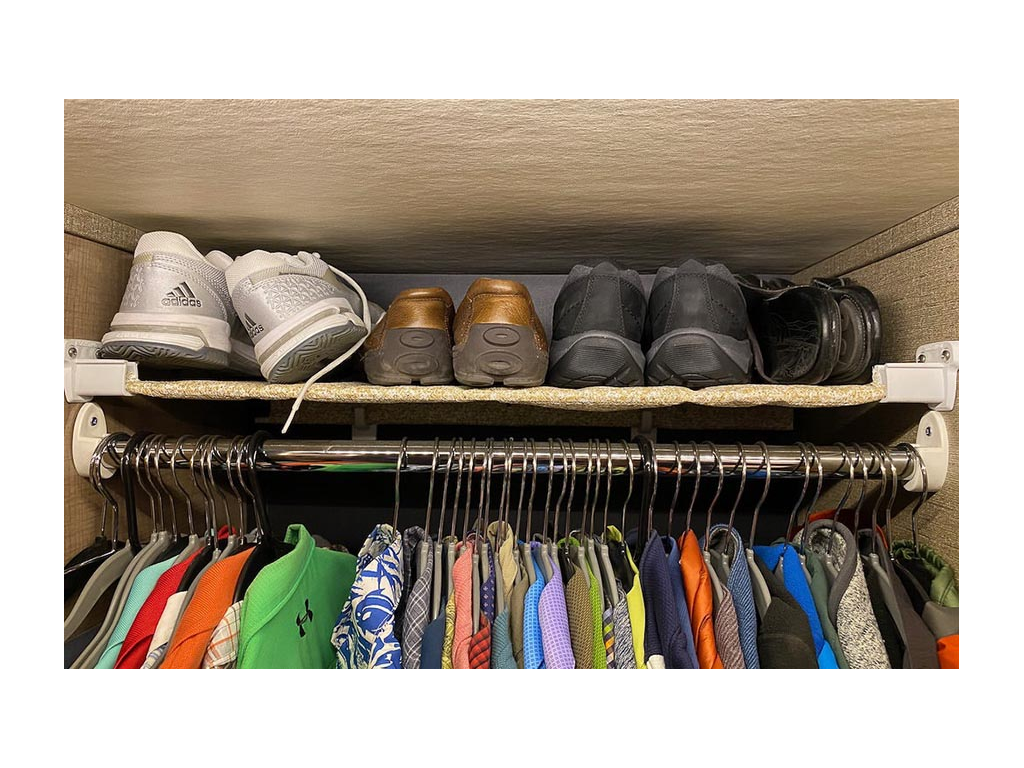 Shoes lined nicely on shelf above hanging clothes in closet