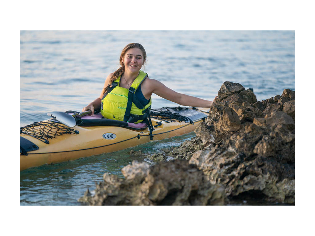 Abby sitting in orange kayak next to rock