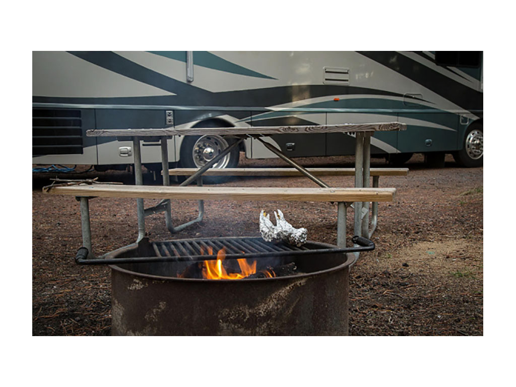 Campfire with picnic table and Winnebago Journey in background 