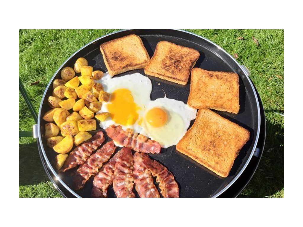 Potatoes, eggs, toast and bacon being cooked on skillet outside