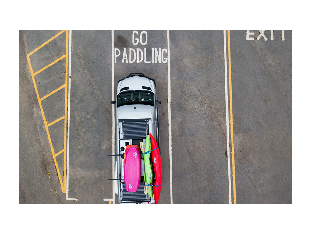 Aerial shot of Revel with kayaks on top parked in parking spot with words "Go Paddling" painted on ground
