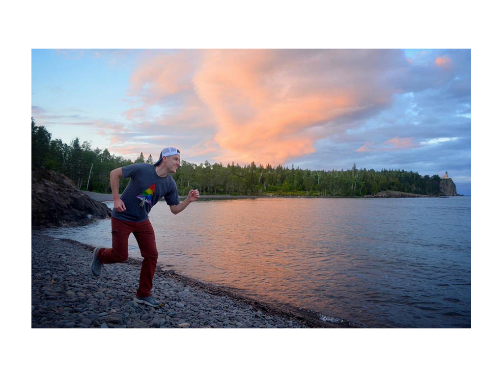 Mikah pretending to run next to water with colorful sky in background. 