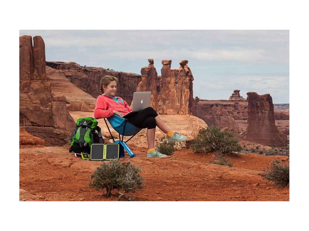 Abby sitting in chair doing homework on laptop with red mountains in background