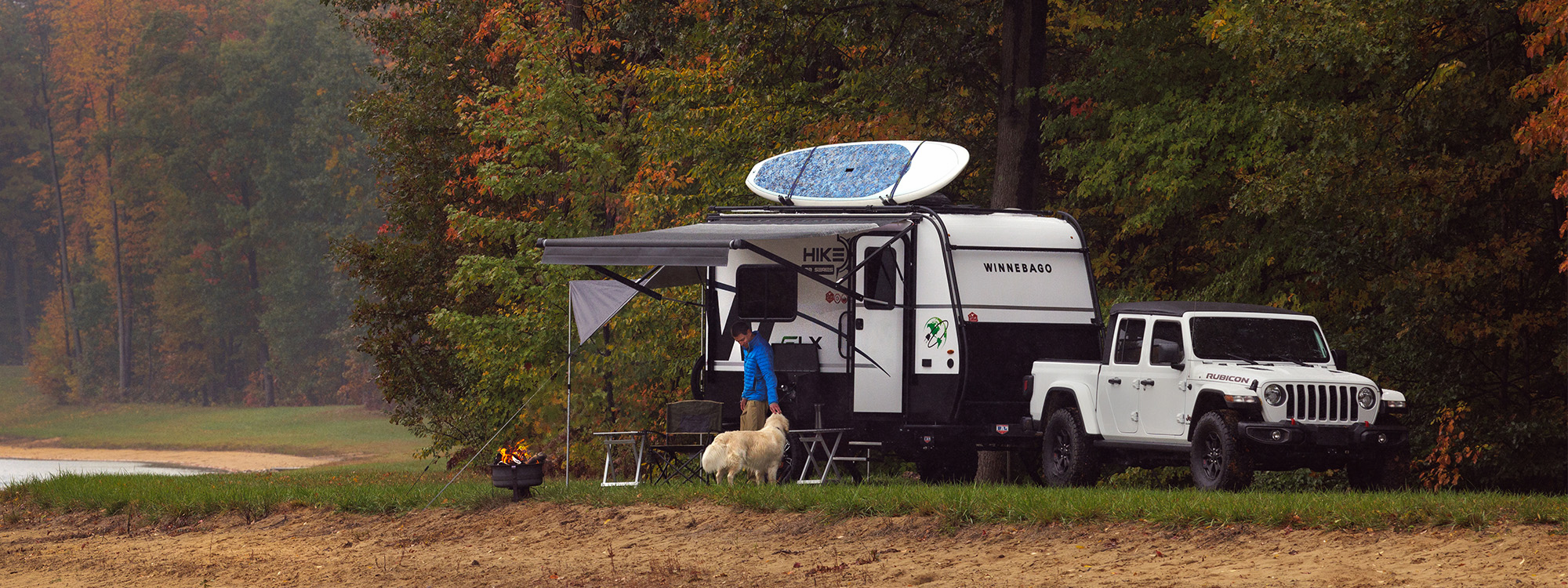 a man and his dog standing outside of the hike 100 flx travel trailer parked on the lakefront