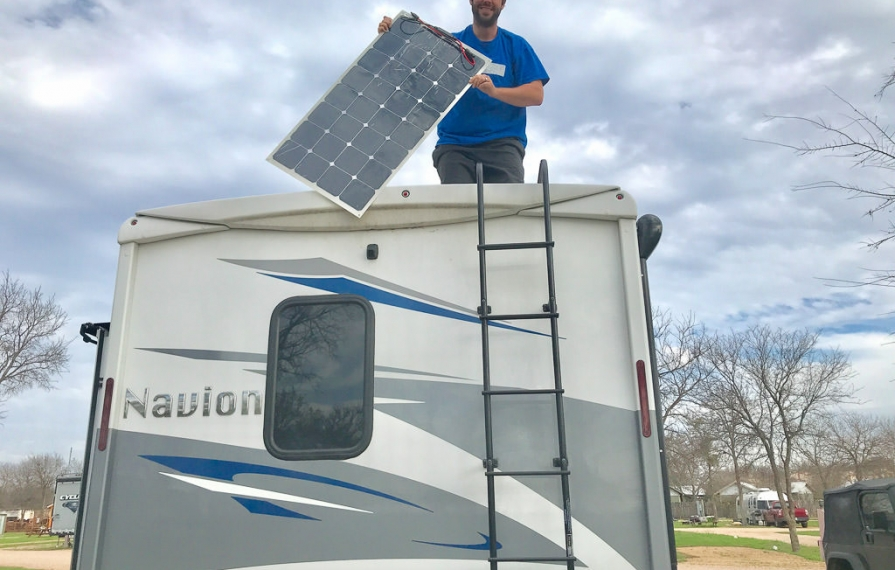 Dan standing on top of Navion holding up a solar panel