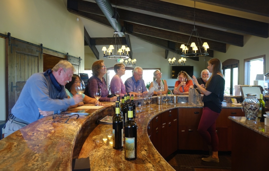 Group of people standing along a bar for a wine tasting.