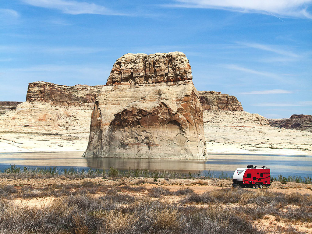 Winnebago Towable parked along the water with large, unique rock formations off shore. 