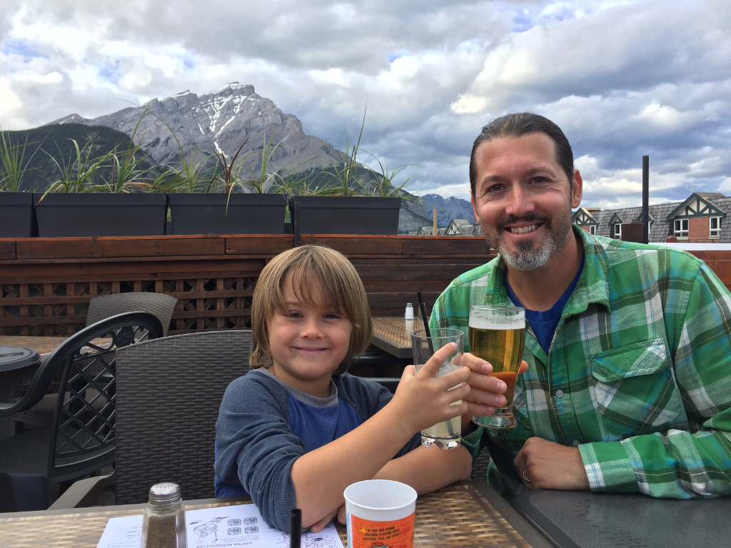 Man and child tapping drinks together on rooftop restaurant in downtown Banff.