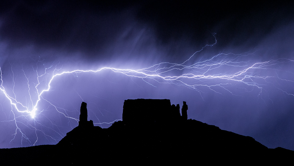 Incredible streak of lightening across the dark sky with the silhouette of rock formations.