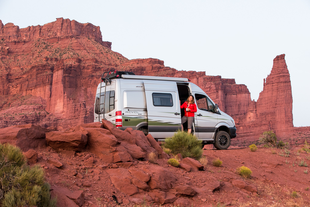 Kathy standing with the side door slightly open on the Winnebago Revel with red rocky canyons in the background.