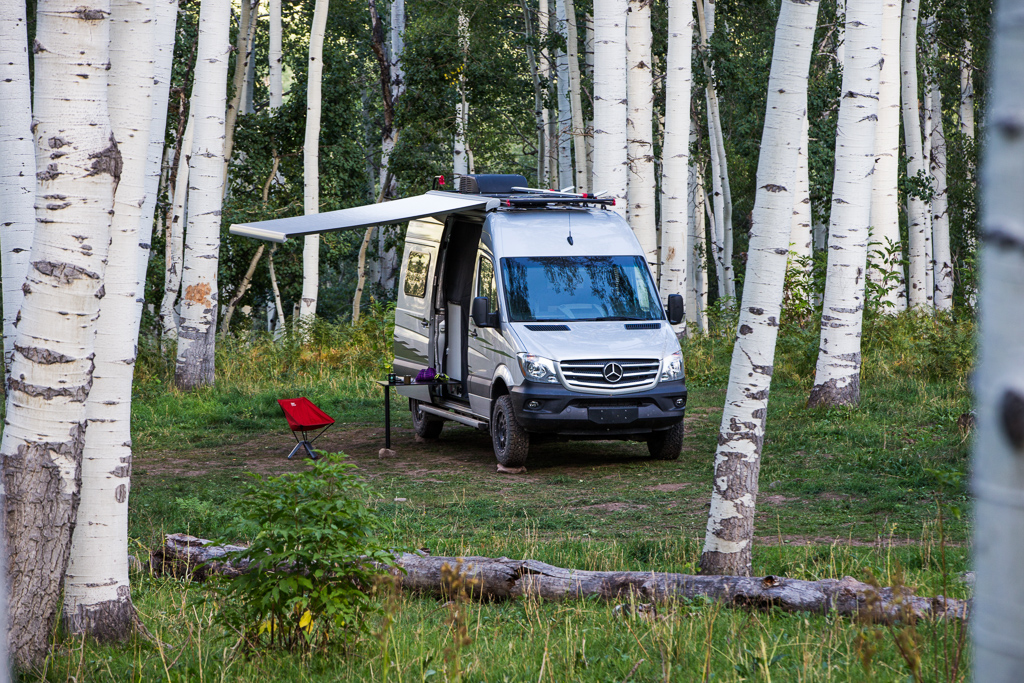 Winnebago Revel parked among trees with awning out.