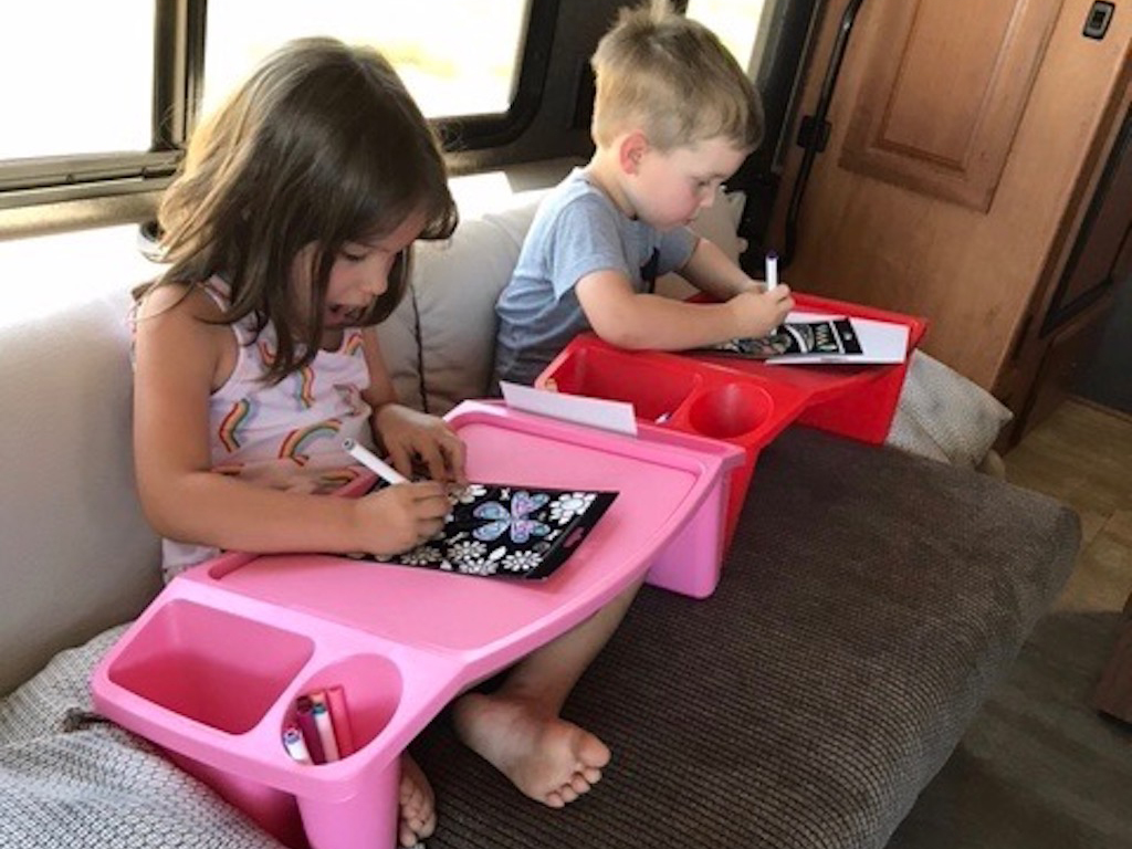 Two kids sitting on couch while coloring on travel trays.