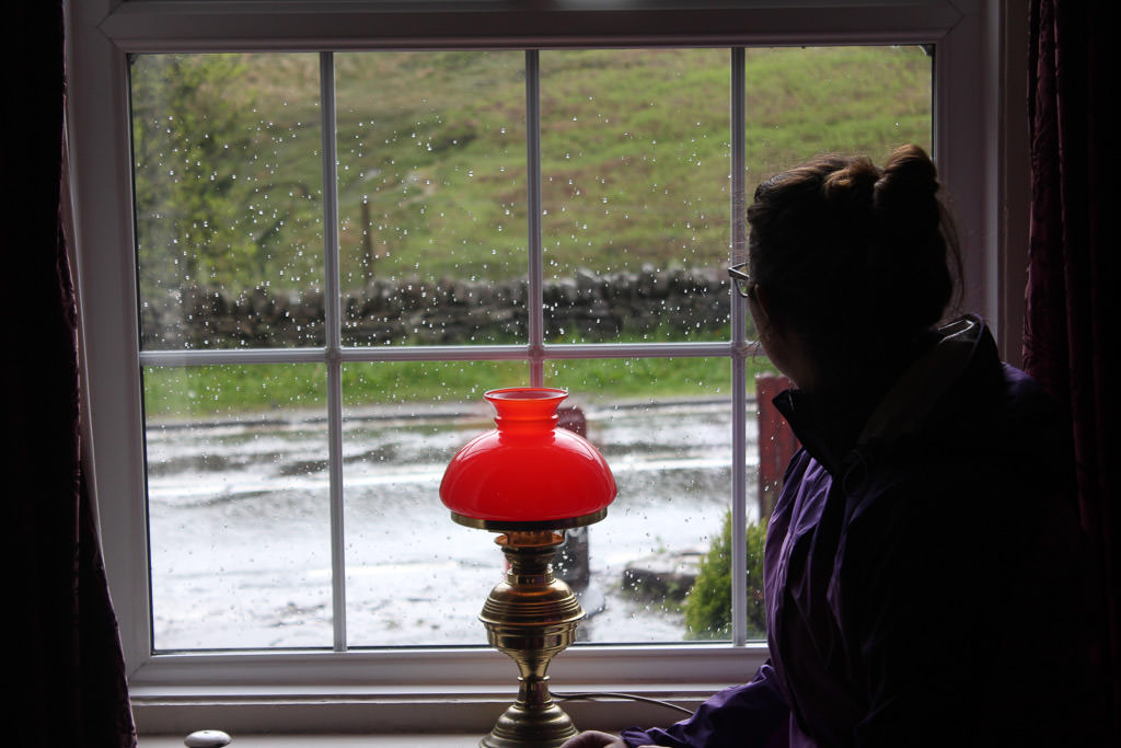 Woman looking out a window to rainy scenery.