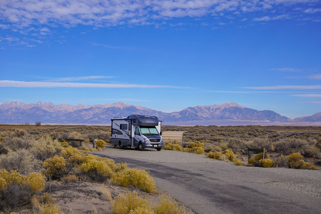 Winnebago Navion parked in campsite with mountains in the background.