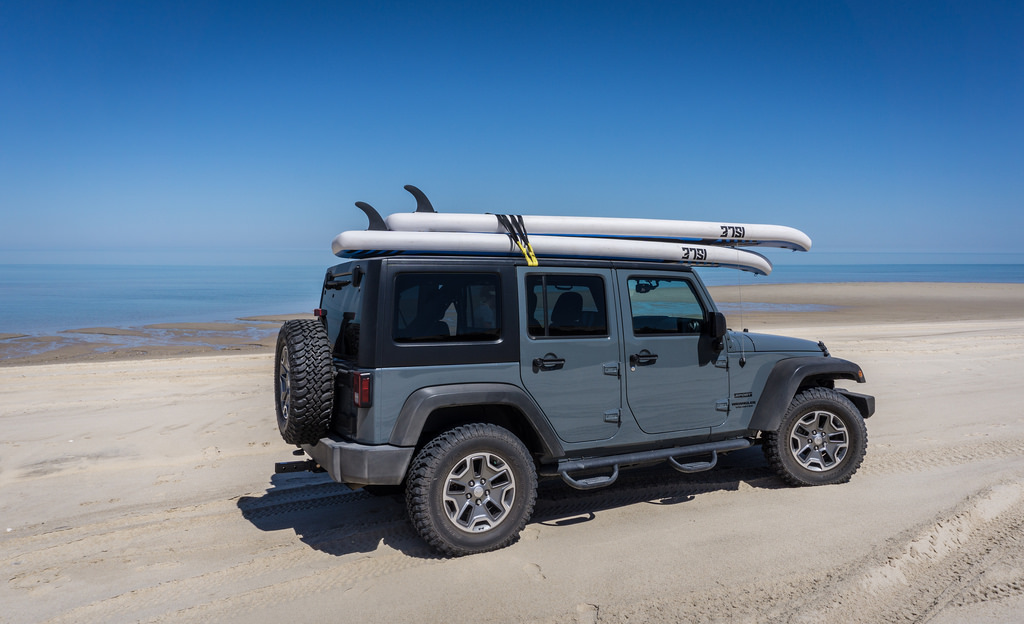 Vehicle parked on the sand with paddle boards on the roof and ocean in the background