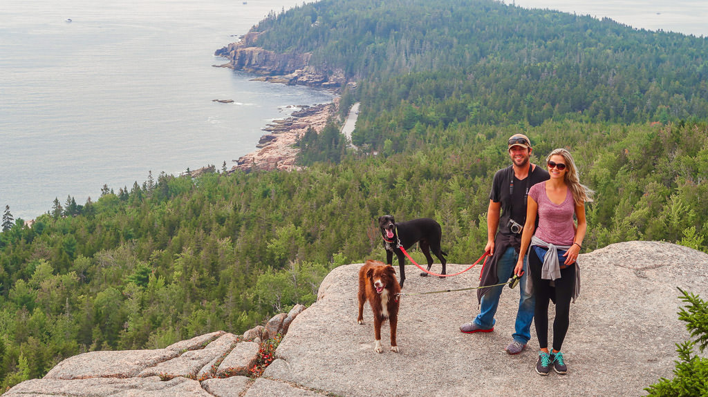 Lindsay, Dan and their two dogs on cliff side with trees and water below