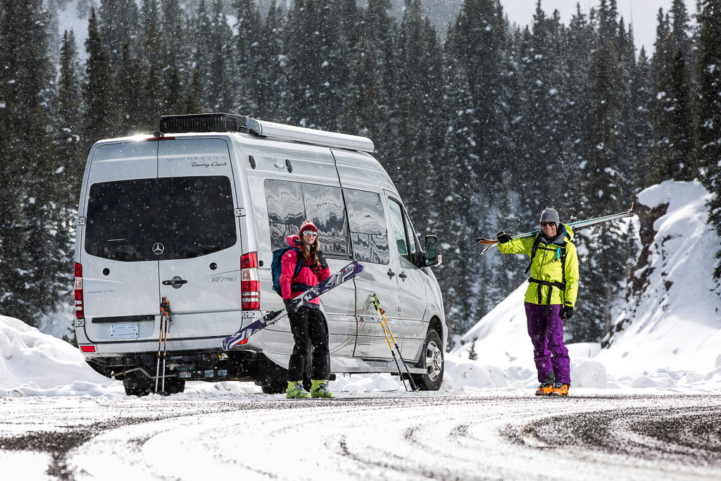 Man and woman holding skis standing outside their Winnebago Era parked on snow covered ground.