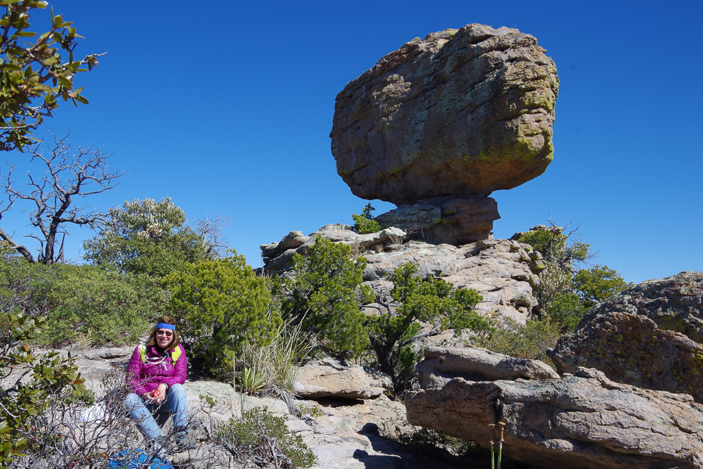 Woman in front of boulder sitting atop rock formation.