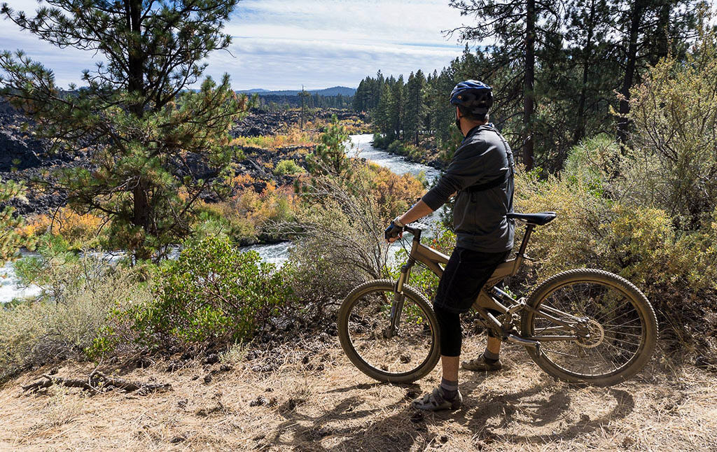 Biker looking out over Deschutes River which is lined with trees.