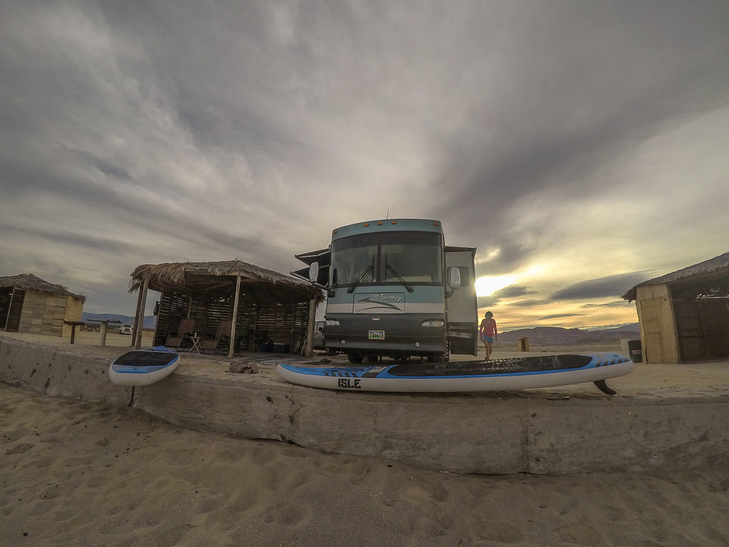 Winnebago Journey parked on sandy campsite with personal palapa and lounge chairs.