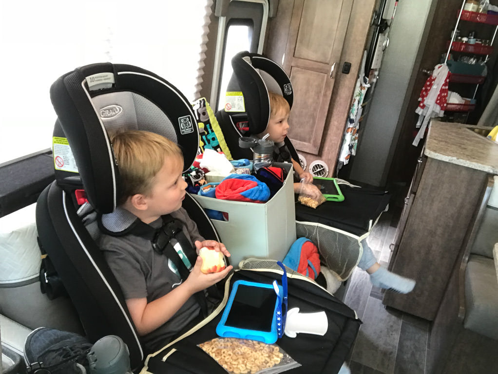 The kids in their car seats in the motorhome with tablets and snacks
