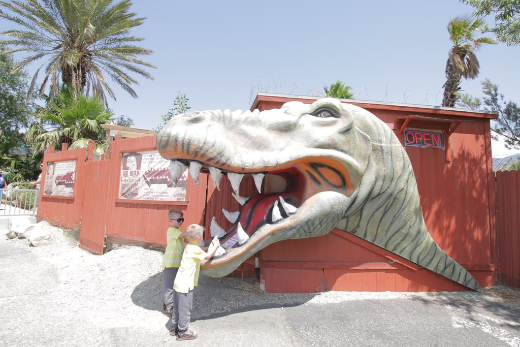 The boys playing by large dinosaur head outside a building