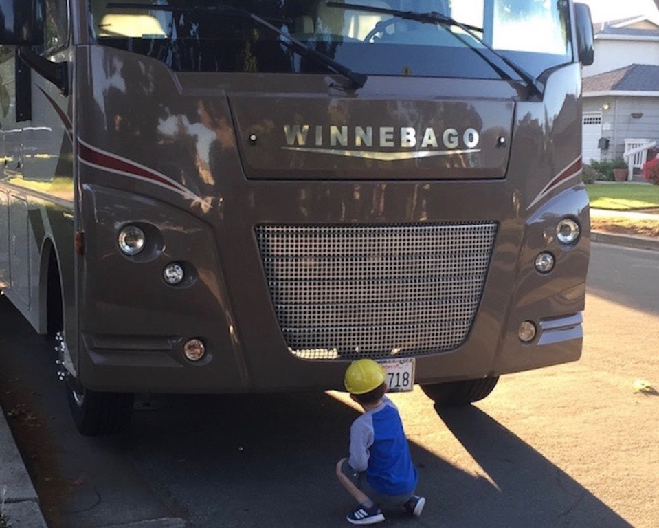 Child kneeling in front of a Winnebago by the front license plate.