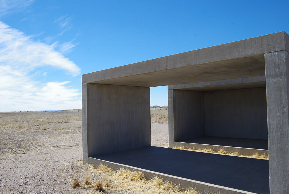 Concrete cube art in the middle of a gravel field.