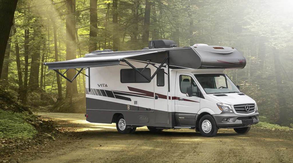 Winnebago Vita with awning out on a dirt road in the woods.