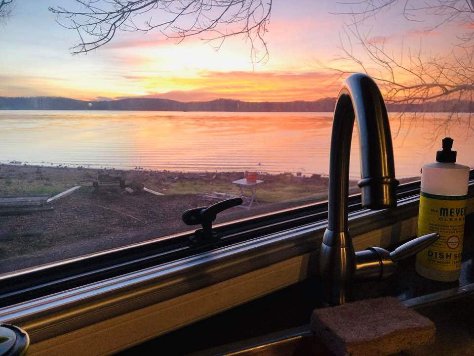 Kitchen sink with colorful sunset over hills out the window.
