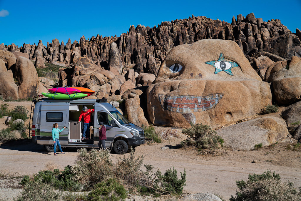 Family coming out of Winnebago Revel that is parked next to unique rock formation that has a face painted on one of the big rocks.