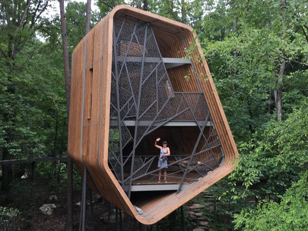 Woman standing in the Bob & Sunny Evans Tree House that appears to be floating among the trees
