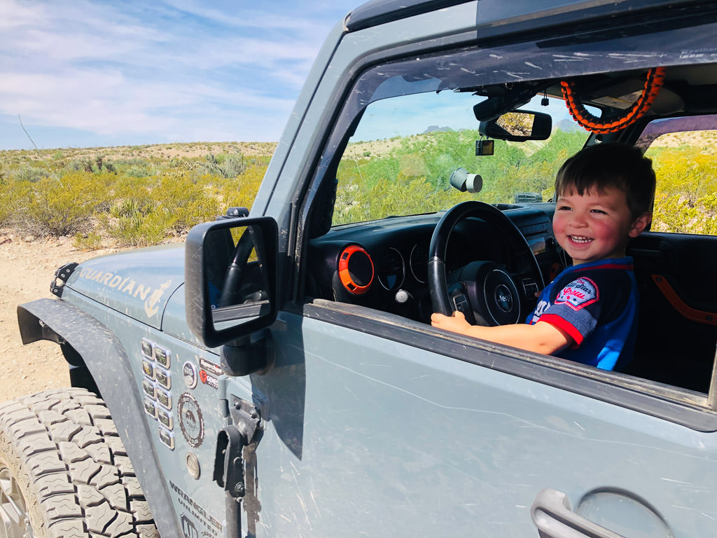 Little boy smiling out the driver side window of parked Jeep.