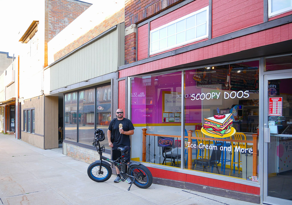 Man poses with foldable electric bicycle in front of ice cream shop