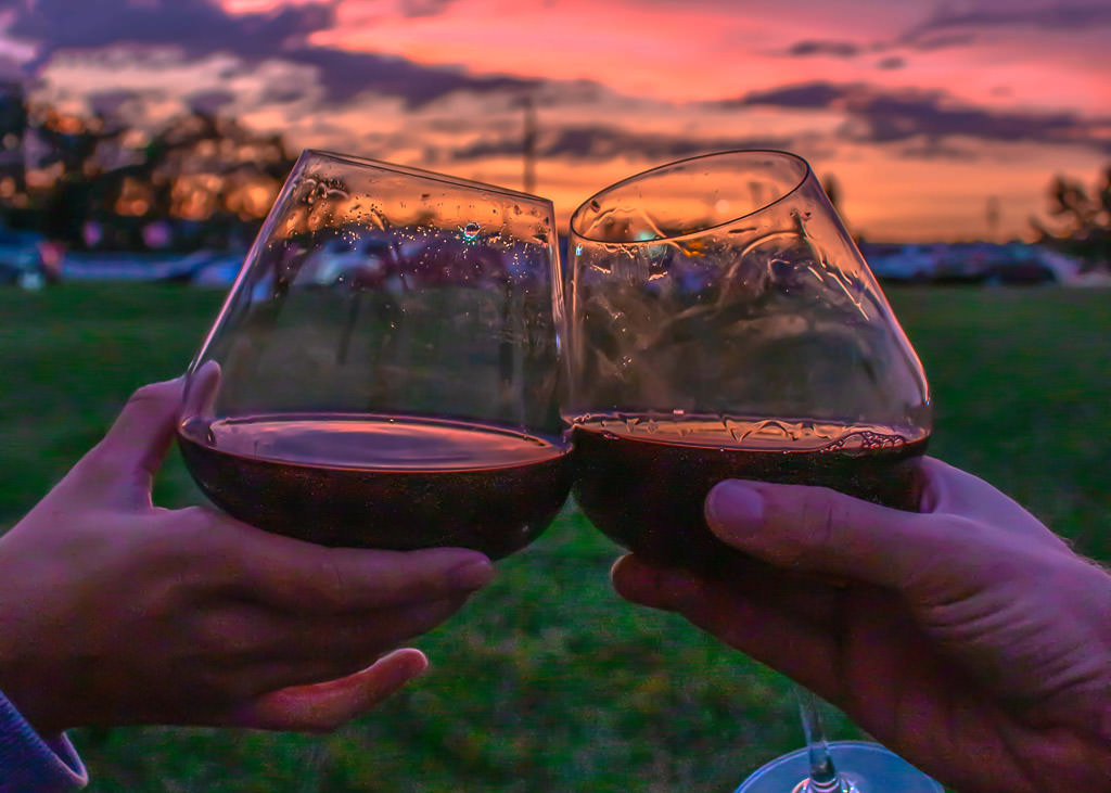 Hands holding glasses of wine with beautiful sunset in background